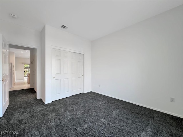 unfurnished bedroom with stainless steel fridge, a closet, and dark carpet