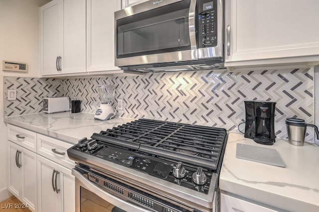 kitchen with light stone countertops, white cabinetry, appliances with stainless steel finishes, and tasteful backsplash