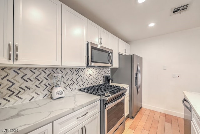 kitchen with white cabinetry, light stone counters, backsplash, light hardwood / wood-style floors, and appliances with stainless steel finishes