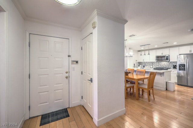 entrance foyer with light wood-type flooring, crown molding, and an inviting chandelier