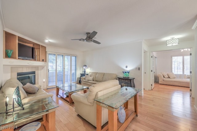 living room with a tile fireplace, light hardwood / wood-style flooring, ceiling fan, and crown molding