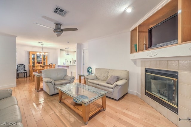 living room with ornamental molding, ceiling fan with notable chandelier, sink, a tile fireplace, and light hardwood / wood-style flooring