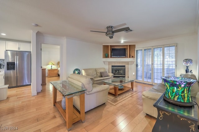 living room with ceiling fan, ornamental molding, a tile fireplace, and light hardwood / wood-style flooring