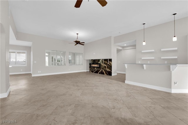 unfurnished living room featuring a stone fireplace and ceiling fan