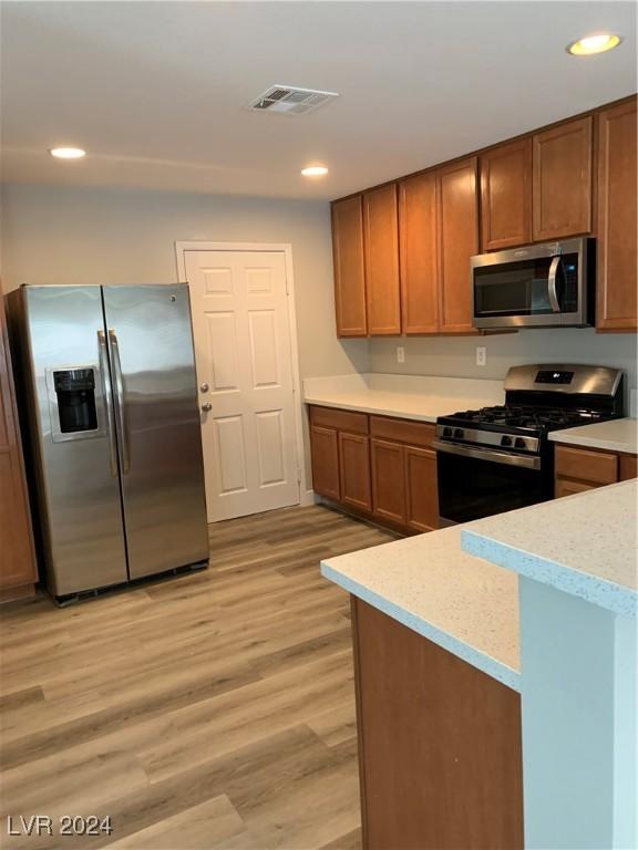 kitchen with light stone countertops, light hardwood / wood-style floors, and appliances with stainless steel finishes