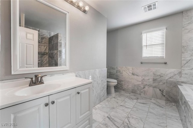 bathroom featuring vanity, a tub to relax in, toilet, and tile walls