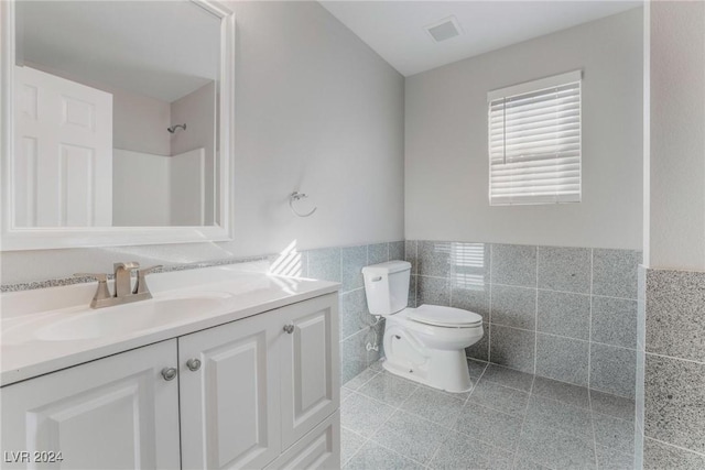 bathroom with vanity, a shower, toilet, and tile walls