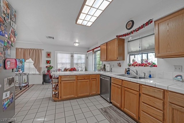 kitchen featuring kitchen peninsula, stainless steel dishwasher, sink, light tile patterned floors, and tile counters