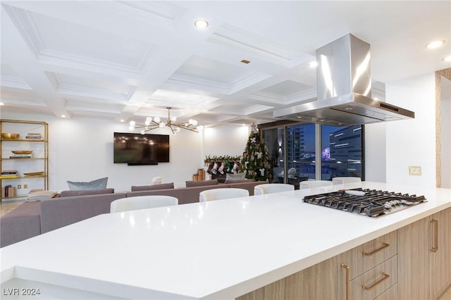 kitchen featuring island exhaust hood, coffered ceiling, stainless steel gas cooktop, beam ceiling, and an inviting chandelier