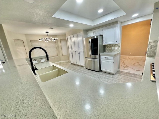 kitchen featuring stainless steel fridge, a raised ceiling, white cabinetry, and sink