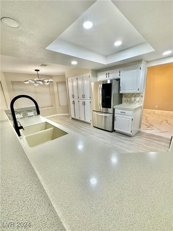 kitchen featuring a raised ceiling, stainless steel fridge, white cabinetry, and sink