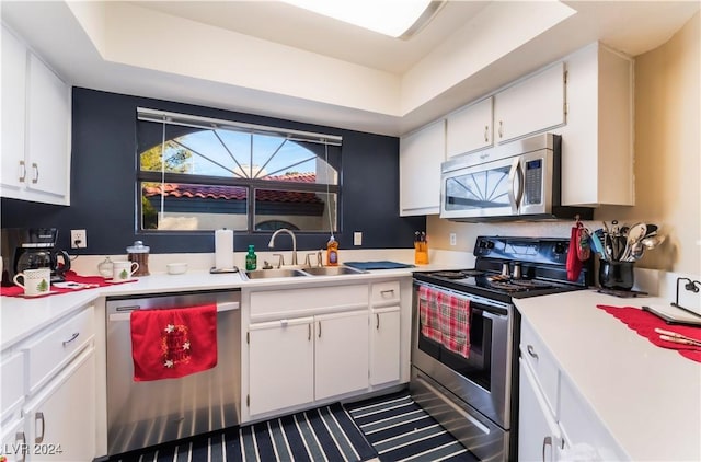 kitchen featuring white cabinets, sink, appliances with stainless steel finishes, and a tray ceiling