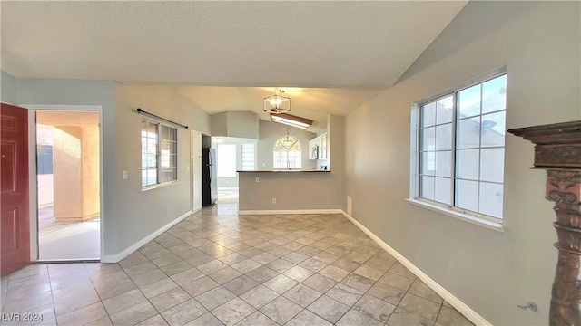 tiled empty room featuring a textured ceiling, vaulted ceiling, and a healthy amount of sunlight