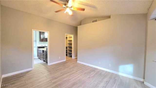 empty room with ceiling fan, light hardwood / wood-style floors, lofted ceiling, and a textured ceiling