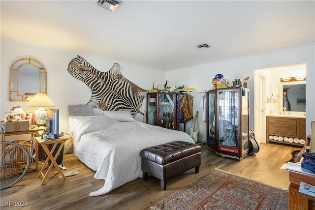 bedroom with hardwood / wood-style flooring, ornamental molding, and ensuite bathroom