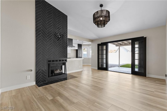 unfurnished living room featuring lofted ceiling, an inviting chandelier, french doors, light wood-type flooring, and a fireplace