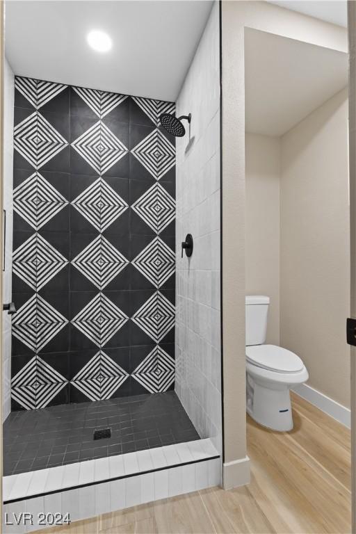 bathroom featuring hardwood / wood-style flooring, toilet, and a tile shower