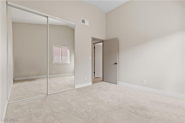 unfurnished bedroom with light carpet, high vaulted ceiling, and a closet