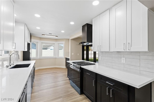 kitchen with wall chimney range hood, sink, light hardwood / wood-style flooring, black gas range oven, and tasteful backsplash