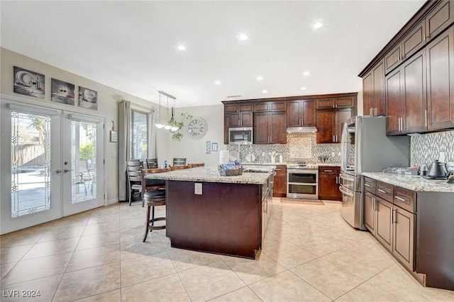 kitchen featuring pendant lighting, french doors, appliances with stainless steel finishes, a kitchen island, and light stone counters