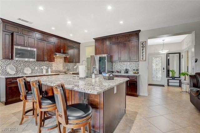 kitchen featuring a kitchen breakfast bar, a kitchen island with sink, light stone counters, and appliances with stainless steel finishes