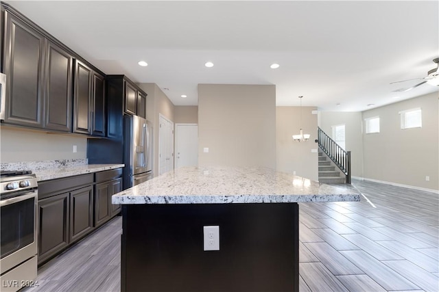 kitchen with pendant lighting, ceiling fan with notable chandelier, a center island, and appliances with stainless steel finishes