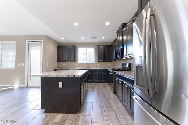 kitchen with light stone counters, sink, a kitchen island, and stainless steel appliances