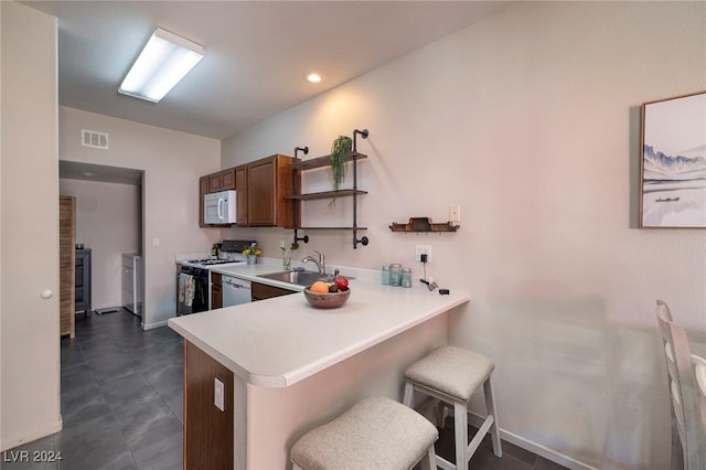 kitchen with sink, dark tile patterned floors, kitchen peninsula, white appliances, and a breakfast bar area