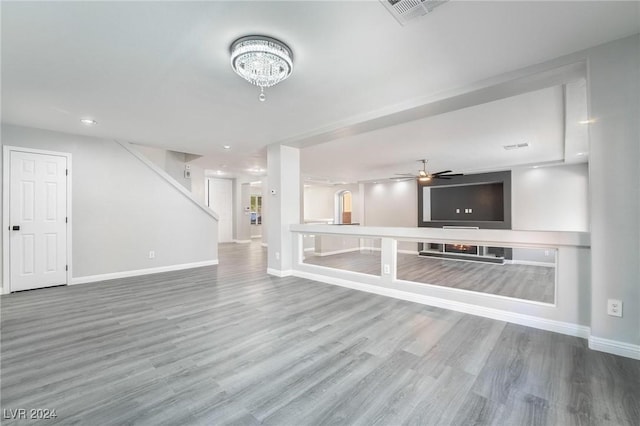 unfurnished living room with ceiling fan with notable chandelier and wood-type flooring