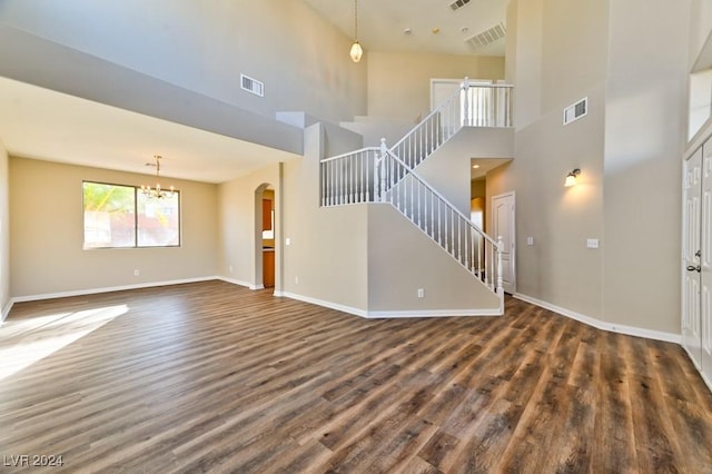 unfurnished living room with a notable chandelier, dark hardwood / wood-style flooring, and a towering ceiling