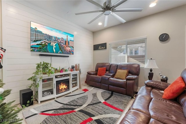 living room featuring ceiling fan, a fireplace, and wooden walls