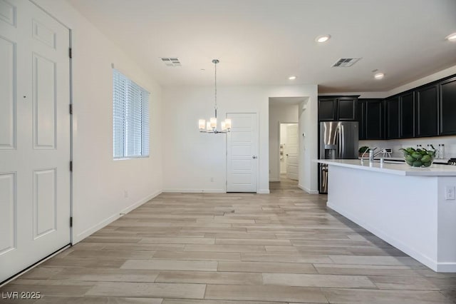 kitchen with sink, hanging light fixtures, stainless steel fridge with ice dispenser, a chandelier, and light wood-type flooring