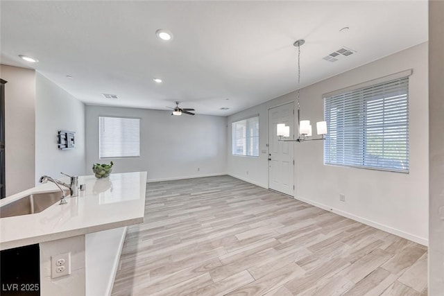 kitchen with ceiling fan with notable chandelier, a sink, visible vents, light countertops, and light wood finished floors