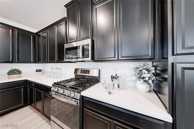 kitchen featuring stainless steel appliances, dark cabinetry, and light countertops