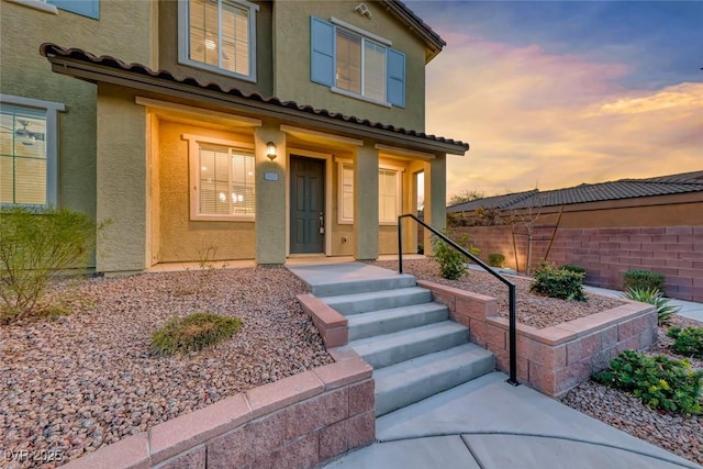 exterior entry at dusk featuring fence and stucco siding