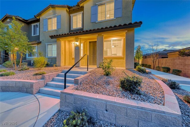 mediterranean / spanish home with a tile roof, fence, and stucco siding