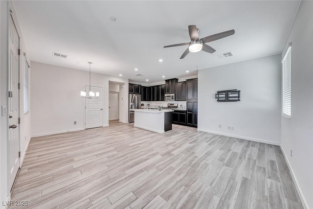 kitchen with light wood finished floors, stainless steel appliances, light countertops, open floor plan, and ceiling fan with notable chandelier