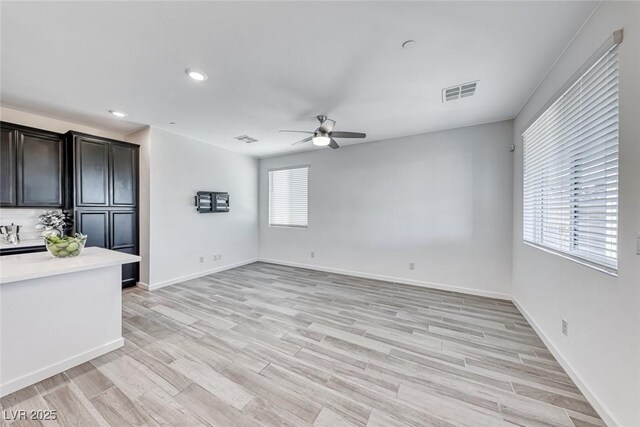 unfurnished living room featuring a wealth of natural light, light wood finished floors, visible vents, and a ceiling fan