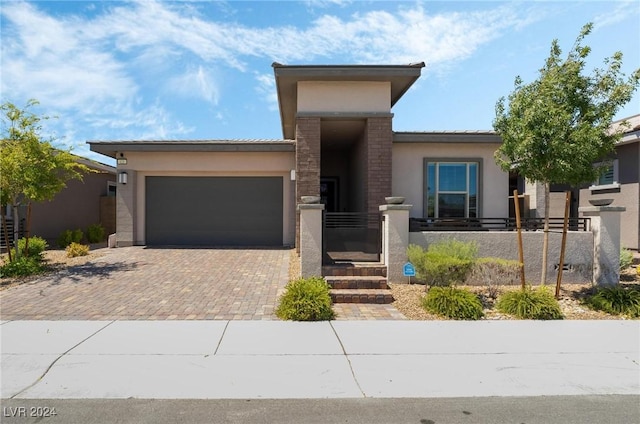 prairie-style house with a garage, decorative driveway, a fenced front yard, and stucco siding