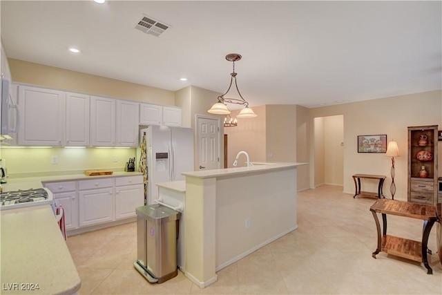 kitchen featuring white fridge with ice dispenser, stove, an island with sink, pendant lighting, and white cabinets