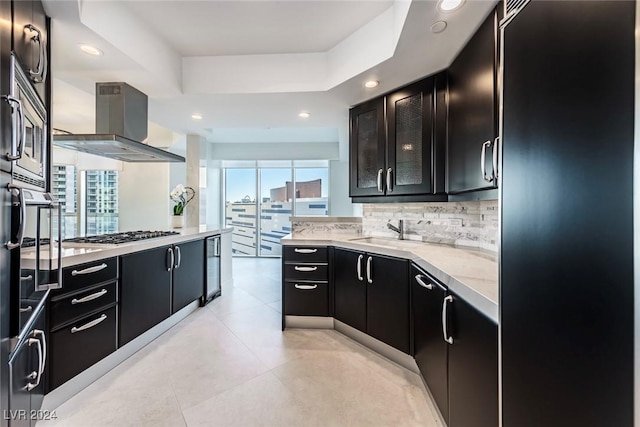 kitchen with backsplash, sink, wall chimney exhaust hood, a tray ceiling, and stainless steel gas cooktop