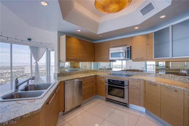 kitchen featuring light stone countertops, sink, a tray ceiling, light tile patterned floors, and appliances with stainless steel finishes