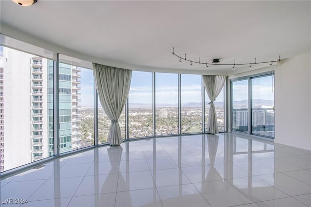 tiled empty room featuring plenty of natural light, track lighting, floor to ceiling windows, and a mountain view