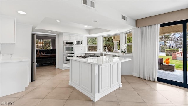 kitchen with white cabinetry, stainless steel appliances, a kitchen island, a raised ceiling, and light tile patterned flooring