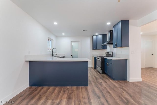 kitchen featuring stainless steel gas range oven, blue cabinets, wall chimney range hood, dark hardwood / wood-style floors, and kitchen peninsula