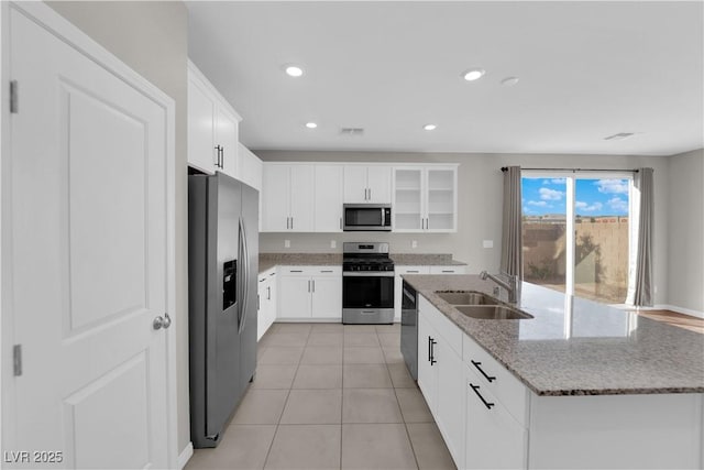 kitchen featuring light tile patterned floors, an island with sink, light stone counters, stainless steel appliances, and a sink