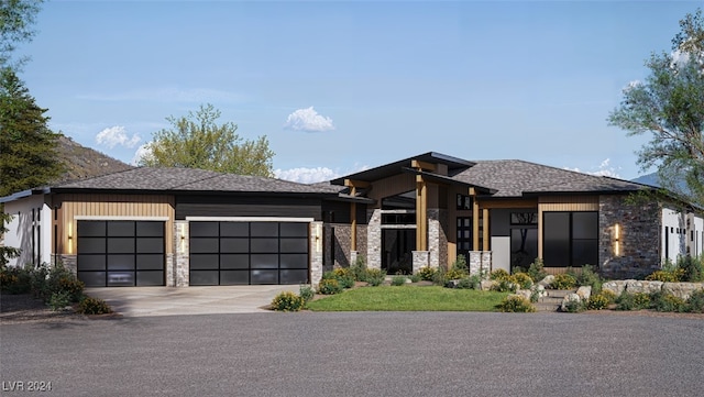 prairie-style house with stone siding, a shingled roof, an attached garage, and driveway