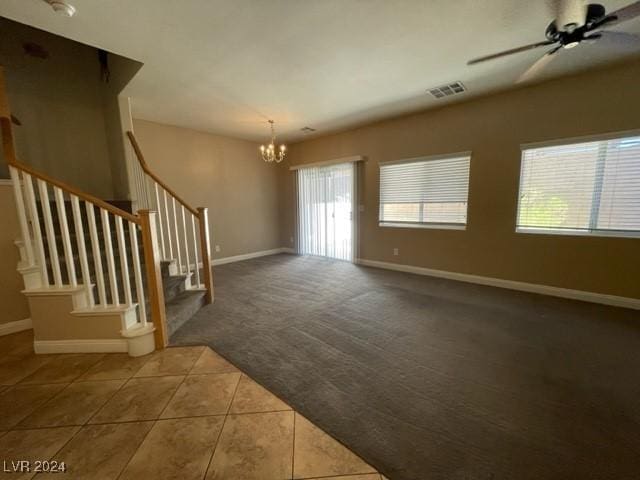 tiled empty room featuring ceiling fan with notable chandelier