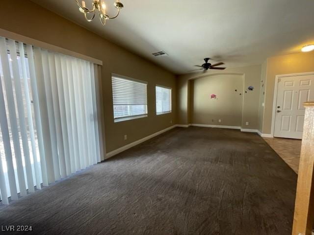 unfurnished living room featuring dark colored carpet, ceiling fan with notable chandelier, and a healthy amount of sunlight