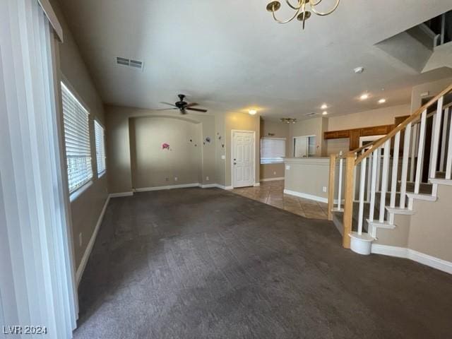 unfurnished living room featuring dark colored carpet and ceiling fan with notable chandelier